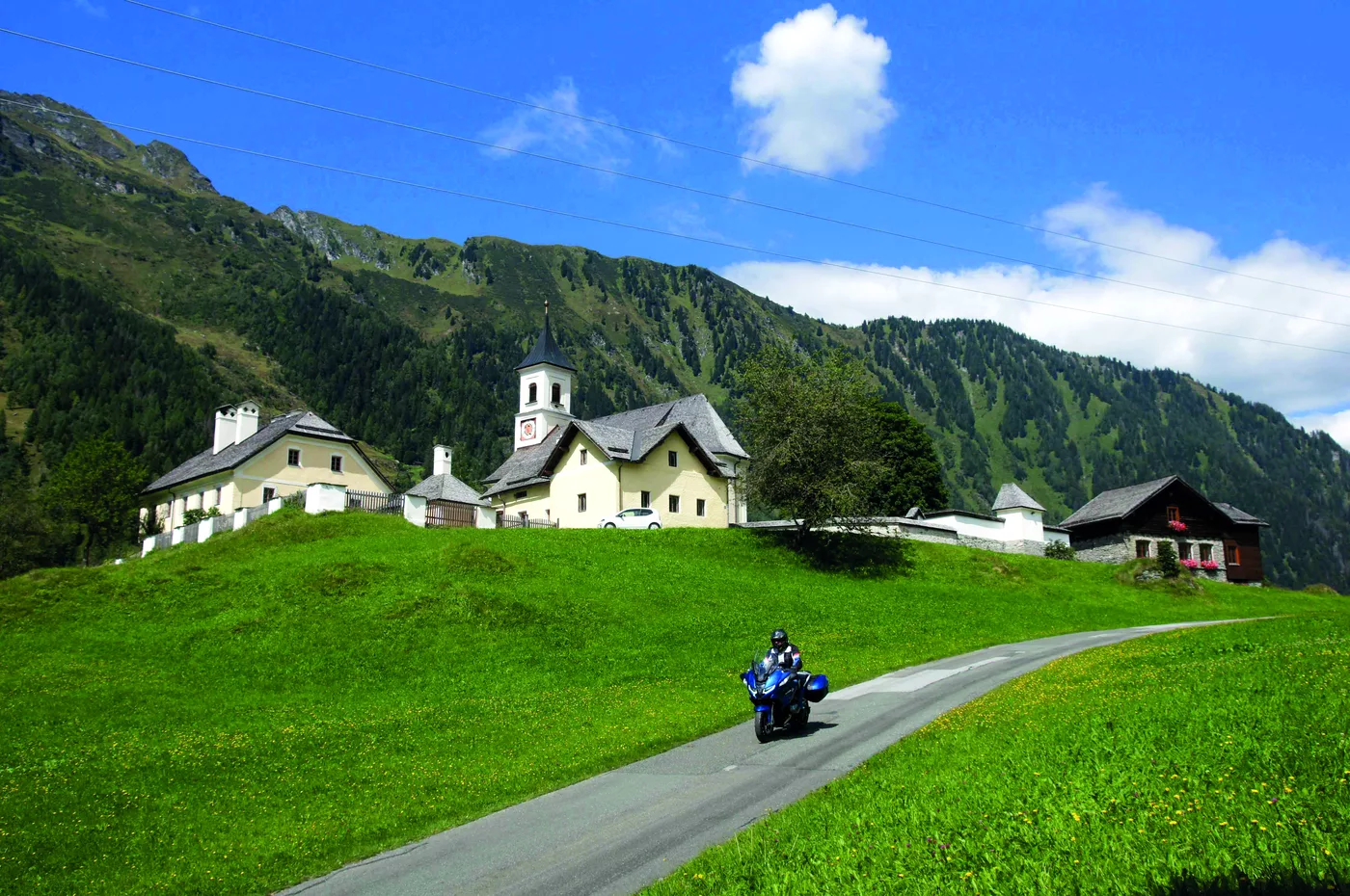 Motorrad auf der Talstraße bei Bucheben, dahinter Kirche und Bergwiesen Motorrad auf der Talstraße bei Bucheben, dahinter Kirche und Bergwiesen